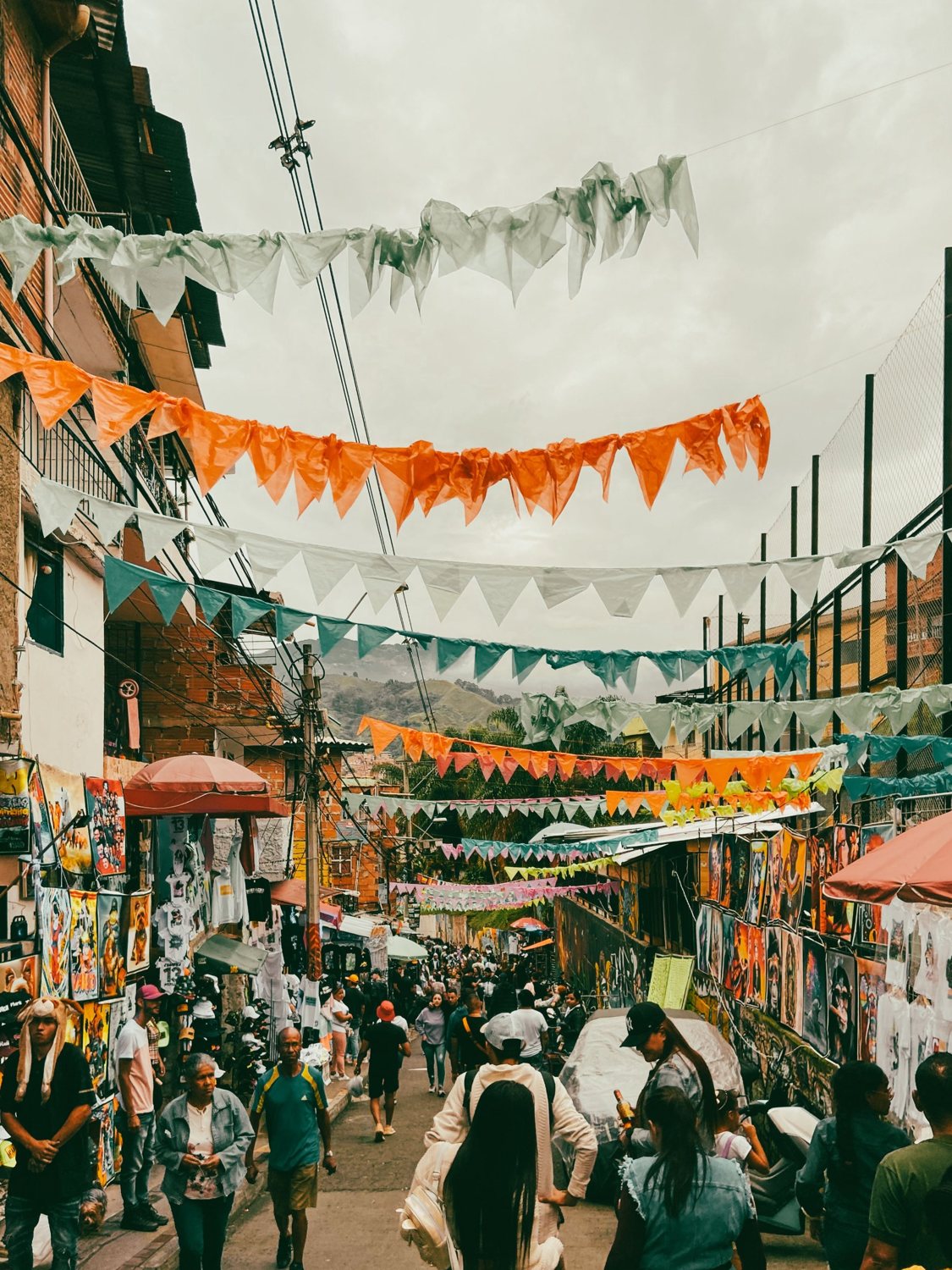 A neighborhood street strung with colorful bunting, with people walking among the stalls