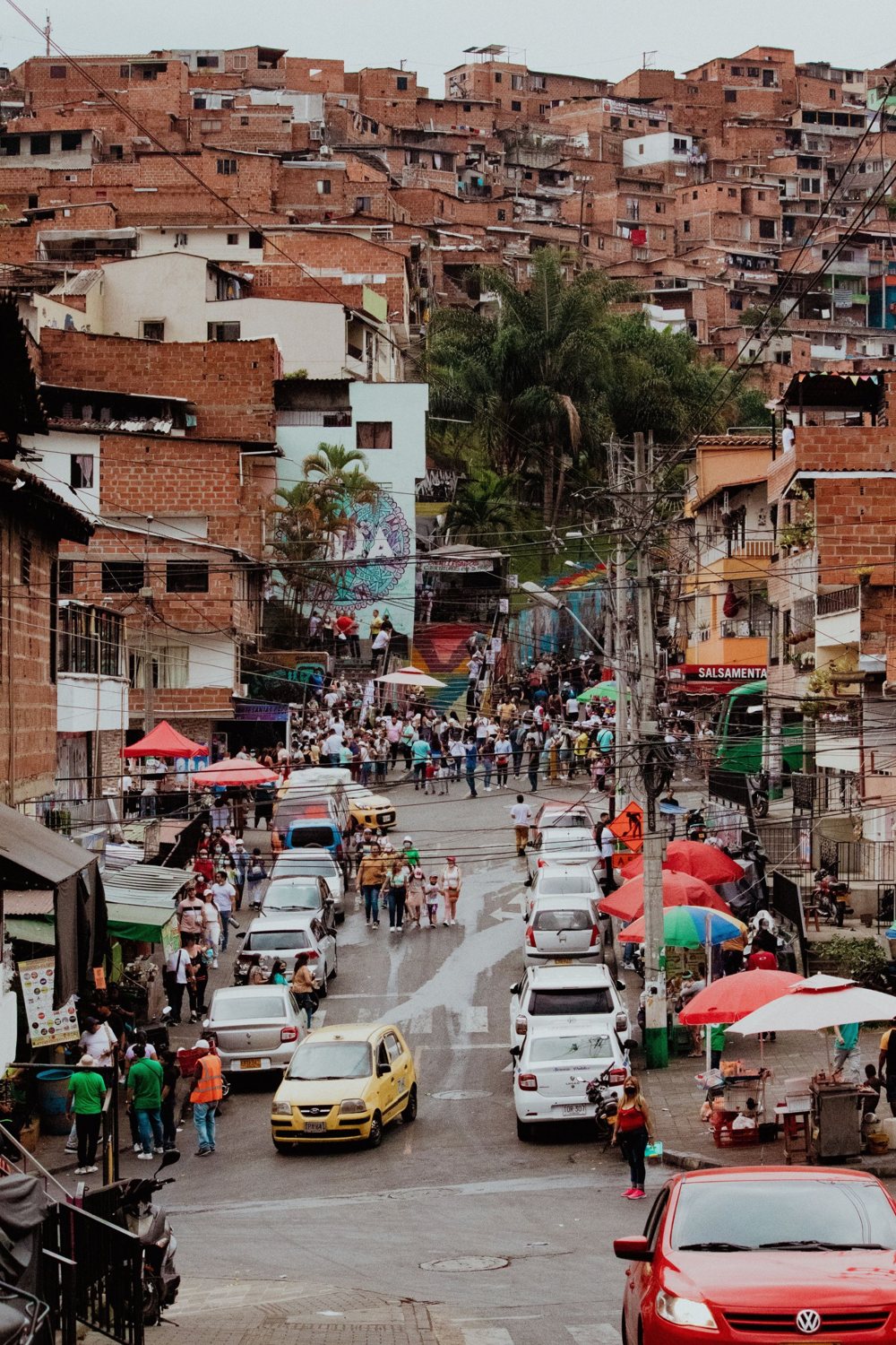 A brick hillside neighborhood, with a street full of people and colorful umbrellas