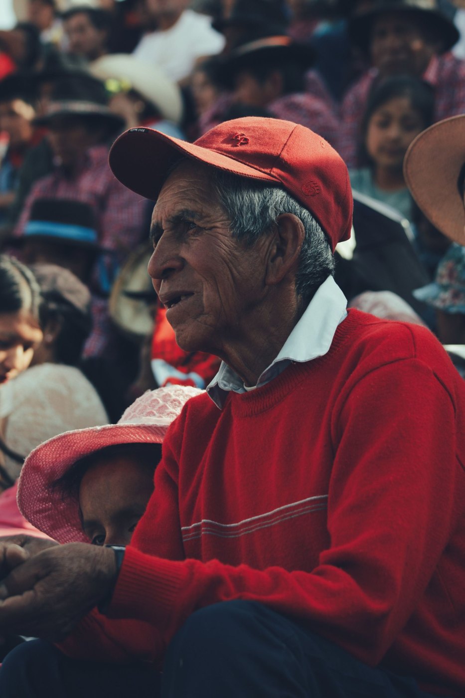 An older man in a red cap and sweater, in the audience at a community gathering